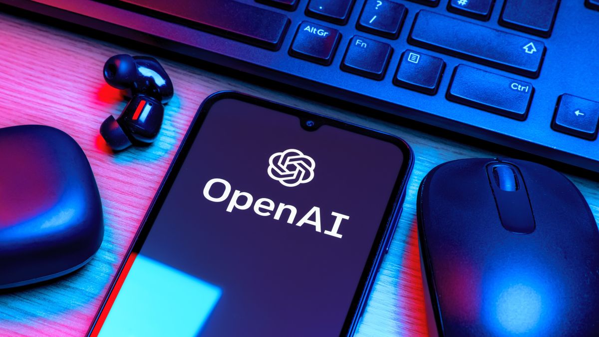 OpenAI logo displayed on a phone next to a keyboard and mouse under blue and red lighting.